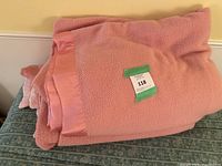 Two pink blankets folded and stacked, showing textured fabric and satin edging.