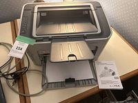 Front view of HP LaserJet printer with paper trays extended, cables connected, and manual placed beside.