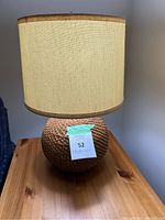 Front view of table lamp showing woven rattan base and beige linen shade on wooden surface.