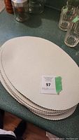 Stack of eight oval white leather placemats on a green countertop, showing texture and edges.