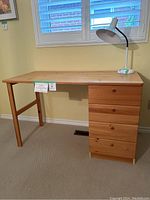 Photo of solid wood desk from front angle showing four drawers and wooden frame, with a lamp on the top left corner.