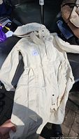 Full view of the cream colored North Face long jacket showing length, sleeves, and front pockets.