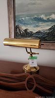 Front view of vintage brass desk lamp on wooden surface with ocean painting in background.