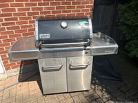 Front view of Weber stainless steel propane grill with closed lid, side shelves and cabinet base