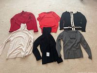 Overview of the six XS sweaters laid out on carpet in various colors and knit styles.
