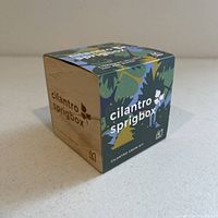 Front and left side view of wooden cube box with colorful botanical patterned sleeve labeled 'cilantro sprigbox'.