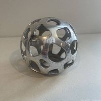 Side view of the chrome openwork sphere sculpture showing smooth chrome finish and irregular openings.