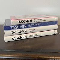 Four TASCHEN books stacked showing spines with titles and publication years.