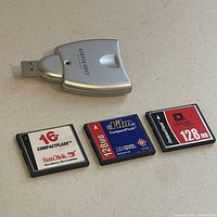 Three CompactFlash cards and one silver USB card reader with flip-out plug arranged on a flat surface.