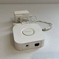 Top view of Philips HUE Bridge showing central button labeled Philips, power adapter with cable.