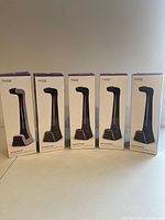 Front view of five boxed Tilted Nation gaming headset stands in a row, four black and one white, showing product branding and packaging.