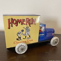 Side view of the tin toy truck, showing the yellow Home Run Chewing Gum box with baseball players graphic and white wheels with text.