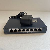 Front view of TP-Link TL-SG108 8 port gigabit network switch showing the ports and power button, with power adapter cable visible on top.