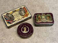 Photo showing the three royal collectable tins: 2 rectangular with King George and Queen Mary themes, 1 round purple Elizabeth II coronation tin.