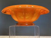 Side view of large orange Davidson cloud bowl on clear stand showing shape and color.