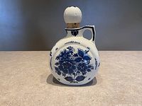Front view of the round moon jug showing blue handpainted floral designs and the corked ceramic lid.