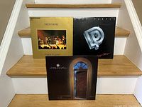 Front covers of the three Deep Purple albums displayed on stairs: 'Made in Japan' double album gold cover with live stage photo, 'Perfect Strangers' black cover with metallic logo, and 'The House of Blue Light' brownish cover featuring a doorway image.