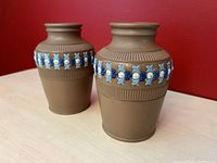 Two matching Doulton Lambeth silicon stoneware vases photographed from an angled side view showing the beige nanotextured body and raised blue and white flower band.