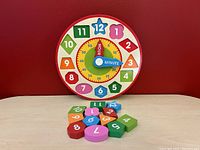 Front view of the Melissa & Doug Shape Sorting Clock toy with colorful number blocks arranged in front of the clock face against a red background.