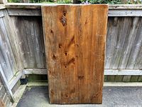 Front view of vintage Puritan pine rectangular rustic table top with visible natural knots and wood grain, set against wooden fence outdoors