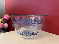 Side view of stacked Pyrex bowls showing blue flower ribbon decoration, clear glass with silver rim on larger bowl.