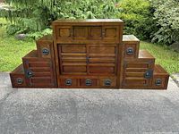 Front view of assembled tansu cabinet showing central block with three top drawers, sliding doors and three bottom drawers flanked by two four-step staircases on driveway
