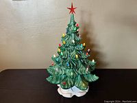 Front view of the ceramic Christmas tree unlit, showing the green ceramic with multiple colored bulbs and white base with red star on top.