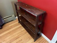 Angled side view of the four tier wooden shelf against a red wall showing structure and condition.