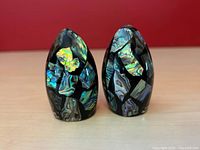 Front view of both salt and pepper shakers showing irregular abalone paua shell inlay in black resin in an egg shape