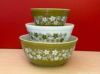 Three nested vintage Pyrex mixing bowls showing the Spring Blossom pattern with white flowers on green and green flowers on white milk glass.