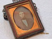 Front view of antique daguerreotype portrait showing a man with dark hair and period clothing inside an ornate rectangular frame with gold and dark textured details.
