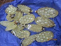 Photo of multiple vintage-style pine cone ornaments in glittery gold finish laid on blue tissue paper inside a box.
