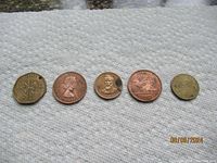 Five coins arranged on a fabric surface showing currency from Ghana, Great Britain, and tokens including Rutherford Hayes and Chuck E. Cheese.