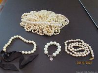 Multiple strands of faux pearl necklaces with one necklace decorated with a black ribbon and a Chico's bracelet.