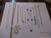 Full view of multiple chain necklaces and pendant necklaces laid out on white background with varied styles.