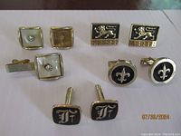 Photo showing various gold-tone and black enamel cufflinks with diverse motifs including lions, fleur-de-lis, initials, and faux diamonds.