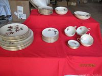 Full set arranged on table showing dinner plates, salad plates, bread plates, cups, saucers, and bowls with autumn leaf pattern and gold trim.