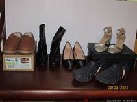 Photo of 5 pairs of shoes including boots, pumps, sandals, moccasins, and woven shoes on a table.