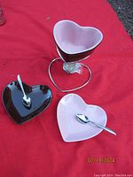 Heart-shaped chocolate fondue pot on metal stand, two heart-shaped dessert plates with small spoons on red cloth