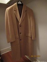 Front view of the Brooks Brothers camel hair top coat hanging on a hanger against a wall.