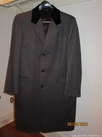 Front view of full-length men's Chesterfield wool top coat, dark gray herringbone pattern, black velvet collar, three buttons, and two welt pockets.