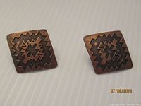Front view of the diamond-shaped copper earrings showing geometric zigzag design.