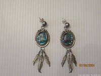 Front view of earrings showing oval turquoise stones with twisted wire accents and dangling silver feathers.
