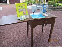 Image showing the sewing machine and wooden cabinet with extension, instruction books and accessories box placed on the cabinet's flap.