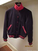 Front view of navy blue varsity university jacket with red collar, cuffs, and pocket trim hanging on Macy’s hanger.