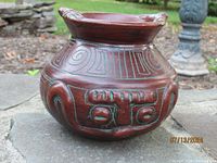 Front view showing red-brown pot with raised turquoise ethnic designs and flared rim with scalloped edges.