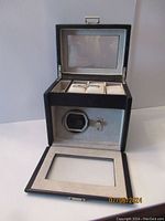 Photo showing the watch winder open with visible interior compartments and watch holder, black and silver finish.