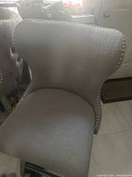 Single gray tufted bar stool with silver button detailing on the backrest edge and winged sides, showing fabric texture and seat cushion.