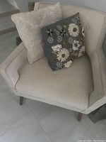 Front angle of off white fabric accent chair with two cushions, visible textured upholstery and wooden legs.