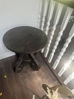 Photo of brown round wood accent table with decorative legs, showing the tabletop surface and part of the base.